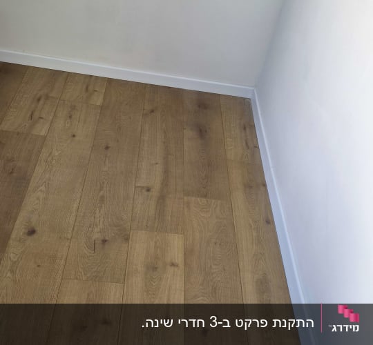 רצפת פרקט במראה עץ אלון מותקנת עם פנלים לבנים בפינת חדר